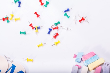 Colorful chalk of red yellow orange violet purple pink green blue chalk pastel colors drawing-pins and fan english alphabet lying on white school desk background copyspace, horizontal photoの写真素材