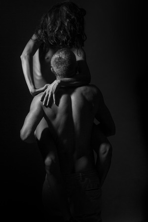 Young stripped pair of sexy woman in trainers sitting on man with strong muscular body standing with back on studio background black and white, vertical pictureの写真素材