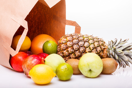 Fresh tropical fruits of pineapple orange juicy grapefruit yellow lemon ripe nectarine purple plum red pomegranate kiwi lime and green apple and paper pack on white background, horizontal pictureの写真素材