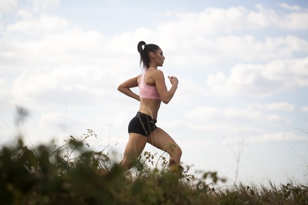 Full length one sexy slim young brunette active girl with straight beautiful body in sportswear on morning running outdoor side view on cloud blue sky background, horizontal pictureの写真素材