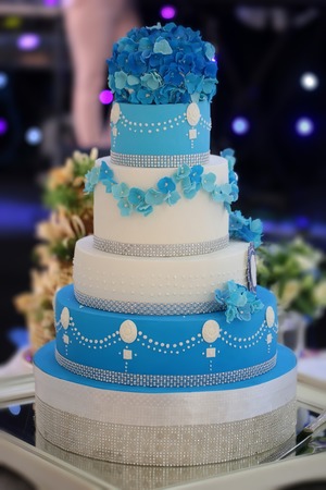 One big beautiful tasty many-tier decorated wedding cake white and blue colours with flower garlad and hydrangea bouquet on top, vertical pictureの写真素材