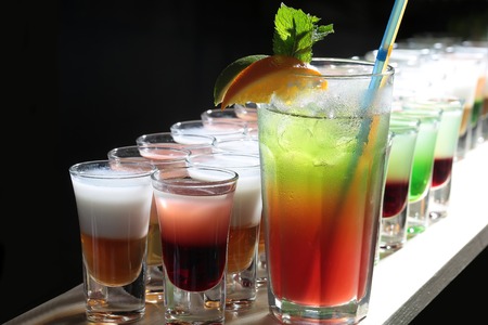 Many beautiful alcoholic shot cocktails in drinking glasses and one long beverage with straws mint...