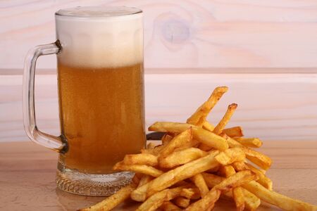 One big glass bocal of light cold delicious beer with white froth and tasty crispy yellow potato fasfood chips on wooden background closeup, horizontal pictureの写真素材
