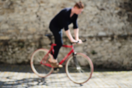 Blurred background of one young active red haired man training on bycicle outdoor sunny day on grey stony wall background, horizontal pictureの写真素材