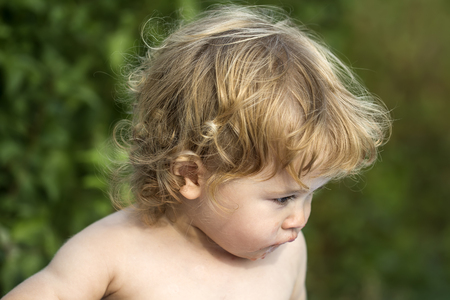 Portrait of one cute small slovenly after eating baby boy with blonde curly hair outdoor in summer on green natural background, horizontal pictureの写真素材