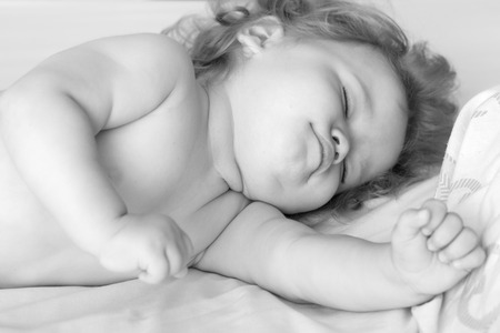 Closeup view of one sweet small sleeping boy child with blonde curly hair round cheeks and tiny fingers lying with closed eyes in bed black and white, horizontal pictureの写真素材