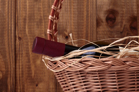 One vintage corked glass bottle of red wine with label decorated with straw lies in gift wicker basket on wooden planks wall background, horizontal photoの写真素材