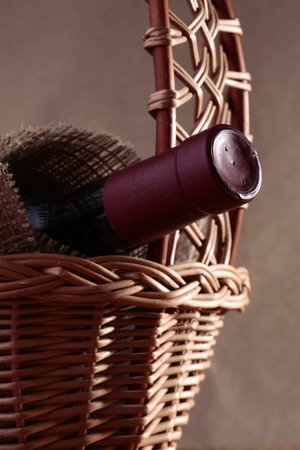 Closeup photo of closed dark glass unlabels bottle of brand red wine covered with burlap in beautiful wicker gift basket, vertical pictureの写真素材