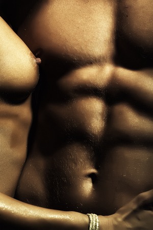 Closeup of naked sensual man with beautiful muscular body and female hand of young woman with bare chest touching male six-pack standing close to each other, vertical pictureの写真素材