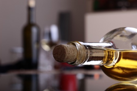 Closeup photo of uncorked bottle of aromatic sweet golden amber color white wine lies on table and another bottle of wine with filled glass on background in kitchen, horizontal pictureの写真素材