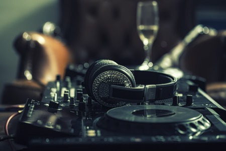 Dj musical mixer professional black console with many buttons and knobs and glamour headphones with pastes in night club or studio on brown leather sofa and wine glass background, horizontal pictureの写真素材