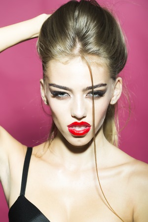Tempting sexual fascinating beautiful blonde young woman with glamorous makeup deep decollete beautiful skin looking straight holding hair studio closeup on pink background, vertical pictureの写真素材