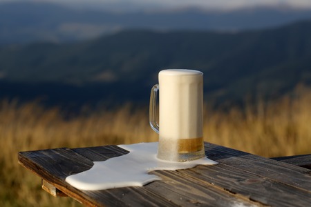 One glass mug with lager or porter tasty frothy beer on wooden table top sunny day outdoor on natural with mountain hills and yellow dry grass background, horizontal pictureの写真素材