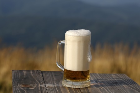 One glass mug with lager or porter tasty frothy beer on wooden table top sunny day outdoor on natural with mountain hills and yellow dry grass background, horizontal pictureの写真素材