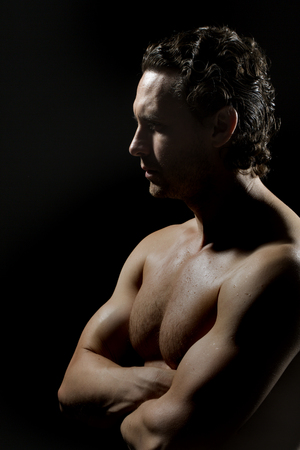 One handsome strong young stripped sweat muscular male model with curly hair and beautiful straight body standing in studio on black background, vertical pictureの写真素材
