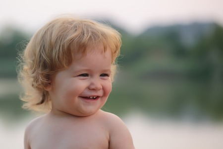 Closeup portrait of one cute funny playful happy smiling little boy with blonde curly hair and round cheeks looking away outdoor on natural background copyspace, horizontal pictureの写真素材