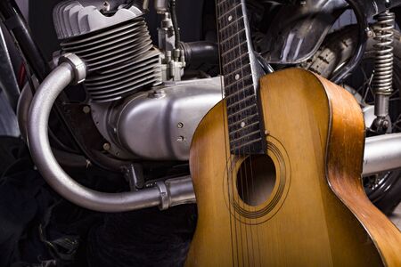 Closeup of one acoustic string light brown color wooden musical instrument of guitar with beautiful shape indoor in studio standing near chrome bike, horizontal pictureの写真素材