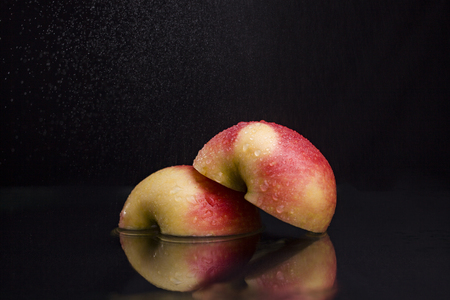 One ripe tasty beautiful seasoning berry fruit of red yellow wet apple cut into two parts with water spray lying in studio on black background, horizontal pictureの写真素材