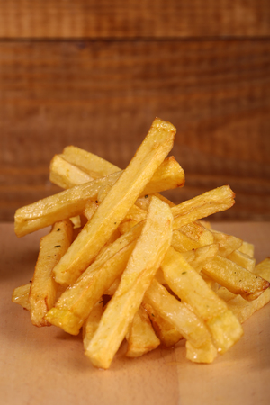 Closeup of fried fresh tasty potato chips sticks golden color lying in heap on wooden background,...