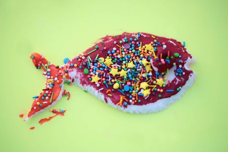 Closeup of one sweet tasty food dessert of colorful candy in icing pink color decorated with different sparkles in shape of fish on green background, horizontal pictureの写真素材