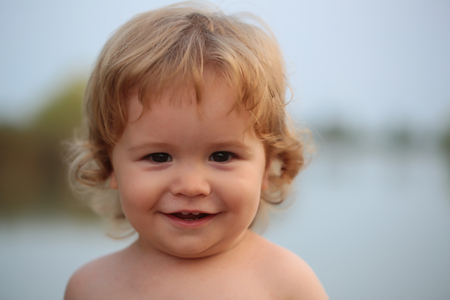 Closeup portrait of one cute funny playful happy smiling little baby boy with blonde curly hair and round cheeks looking forward outdoor on natural background, horizontal pictureの写真素材