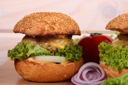 One big tasty appetizing fresh burger of green lettuce red tomato cheese bacon slice meat cutlet violet oinion and white bread bun with sesame seeds on wooden table closeup, horizontal pictureの写真素材