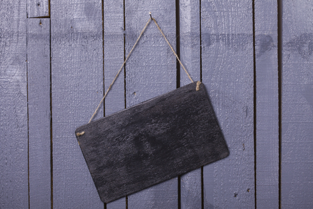 Closeup of one empty door plate or tablet of brown wood with time information for visiting hanging on rope indoor in studio on gery wooden backdrop copyspace, horizontal pictureの写真素材
