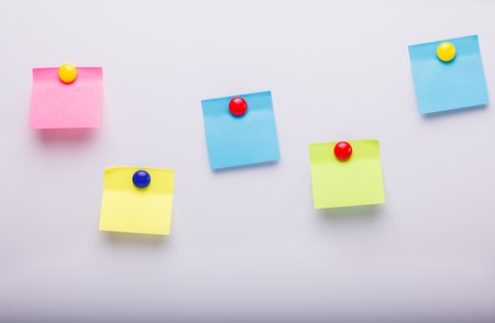 Closeup view of five empty colorful paper stikers pink yellow and blue colors hanging on white flat blank wall copyspace with no people, horizontal pictureの写真素材