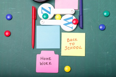 Closeup view of school equipments of paper sheet with homework and back to school text alphabet colorful chalk in office cup red pen on green blackboard with no people copyspace, horizontal pictureの写真素材