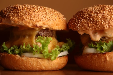 Big tasty appetizing fresh burgers of green lettuce red tomato cheese and bacon slice meat cutlet and white bread bun with sesame seeds closeup, horizontal pictureの写真素材