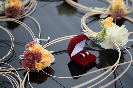 Red velvet box with two wedding golden rings standing on black glossy background with decorative...