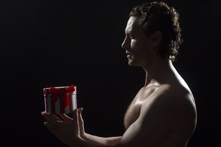 Side view of one handsome sexy strong muscular young man with bare chest and curly hair standing...