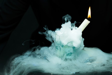 Closeup view of one thin burning with yellow fire candle in glass with lush white smoke in studio on black background, horizontal pictureの写真素材