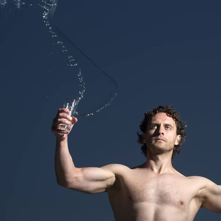 One young handsome unshaven muscular strong man with curly hair bare chest holding glass with...