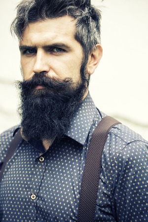 Closeup view of one handsome senior stylish man with black hair and long lush beard in blue shirt...