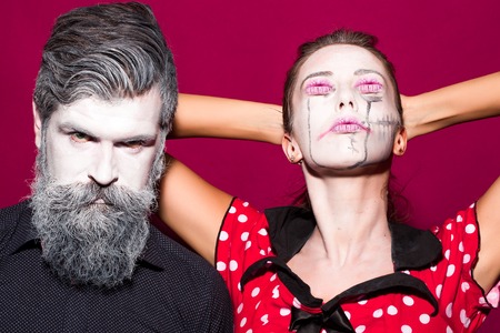 Closeup view of couple of painted halloween holy chrackters woman in red dress with lips eyes and man with long lush beard looking forward on studio purple wall background, horizontal pictureの写真素材