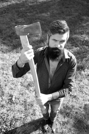 Top full length view of one handsome strong stylish male logger of young man with long lush beard and moustache in shirt holding wooden axe standing on grass outdoor black and white, vertical pictureの写真素材
