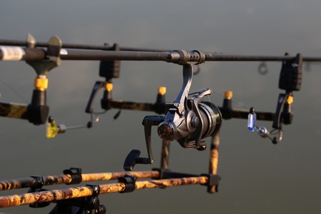 Closeup silhouette of fish-tackle fishing rods reel and rings with gray blurred natural water background, horizontal pictureの写真素材
