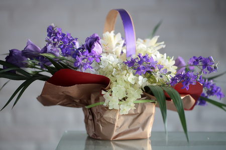 Closeup beautiful bunch of fresh tender white and violet flowers mixed decorated with green leaves in paper packet with handle on glass table on blurred gray background, horizontal pictureの写真素材