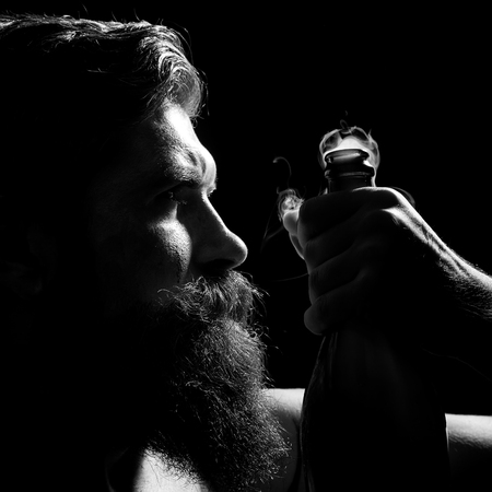 Closeup portrait side view of one senior serious man with long lush beard holding uncorked glass champagne wine bottle with smoke in studio on black background, square pictureの写真素材