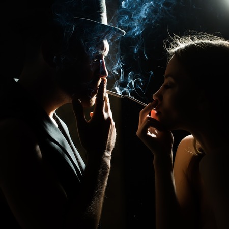 Couple smoking cigarettes face to face beautiful young woman and bearded man wearing hat waistcoat...