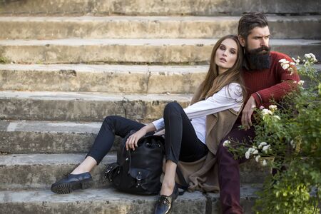 One beautiful stylish couple of young woman and senior man with long black beard sitting embracing close to each other outdoor in autumn street on stairs sunny day, horizontal pictureの写真素材