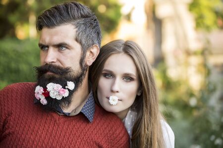 Young beautiful couple of woman and man with long black beard with many little white red and pink flowers sunny day outdoor on natural background, horizontal pictureの写真素材