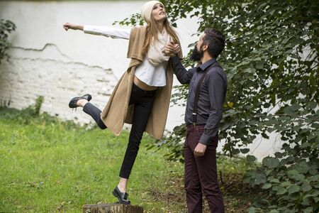 Beautiful young fashionable emotional expressive couple of slim woman and man with long lush black beard standing together on fresh green grass outdoor on autumn natural background, horizontal pictureの写真素材