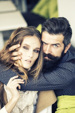 Closeup view on one attractive stylish emotional couple of young woman and senior man with long black beard embracing sitting close to each other intdoor in cafe, vertical pictureの写真素材