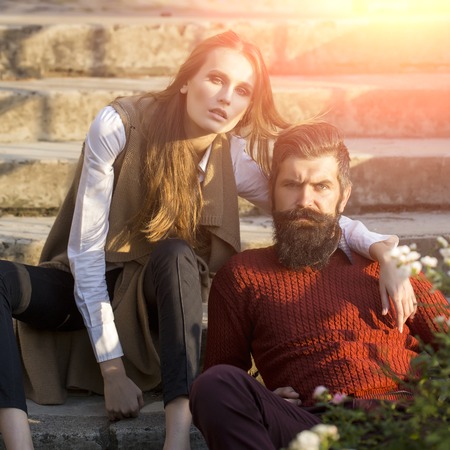 One beautiful stylish couple of young woman and senior man with long black beard sitting embracing close to each other outdoor in autumn street on stairs sunny day, square pictureの写真素材
