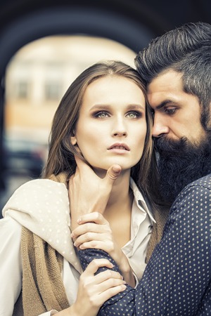 One beautiful stylish couple of young woman and man with long black beard standing close to each other outdoor in autumn street near arch, vertical pictureの写真素材