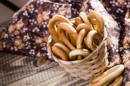 Photo top view of hard oval cracknels in basket heaped high with some bagels lying on wooden table over blurred flowery cloth rustic background, horizontal pictureの写真素材