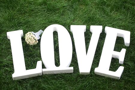 Closeup view of one beautiful fresh bright white yellow big wedding bouquet of rose flowers and love text of letters lying on green grass, horizontal pictureの写真素材