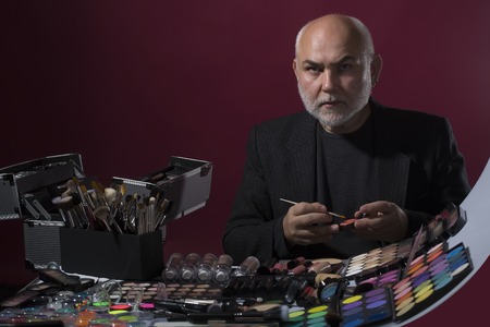One professional male visagiste with many different natural brushes for eyeshadow powder and facial foundation and big colorful set doing makeup on purple background, horizontal pictureの写真素材
